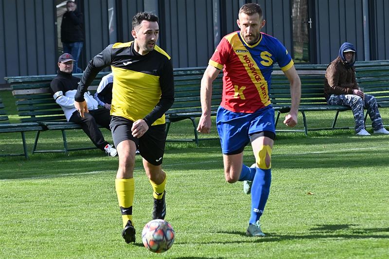 Na snímku z utkání s Nošovicemi je v souboji s jedním z hráčů soupeře domácí útočník Lukáš Polášek (ve žlutém), právě po faulu na něj následovala vítězná penalta domácích.